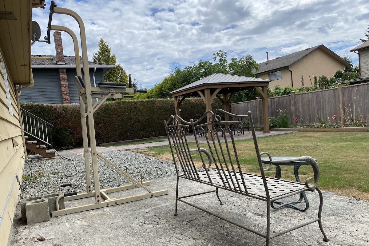 A patio with a metal bench, a pergola, and a gravel area.