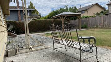 A patio with a metal bench, a pergola, and a gravel area.