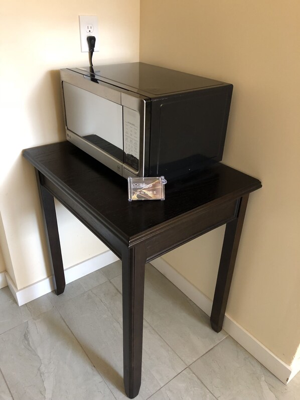 A black table with a microwave on top, a power outlet, and a clear plastic item on the table.