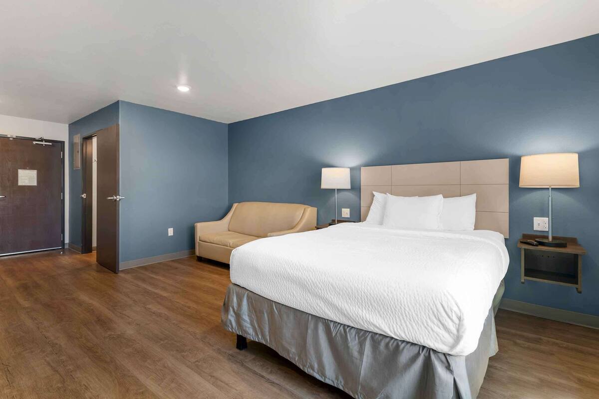 A hotel room with a large bed, a sofa, two bedside lamps, and a wooden floor.