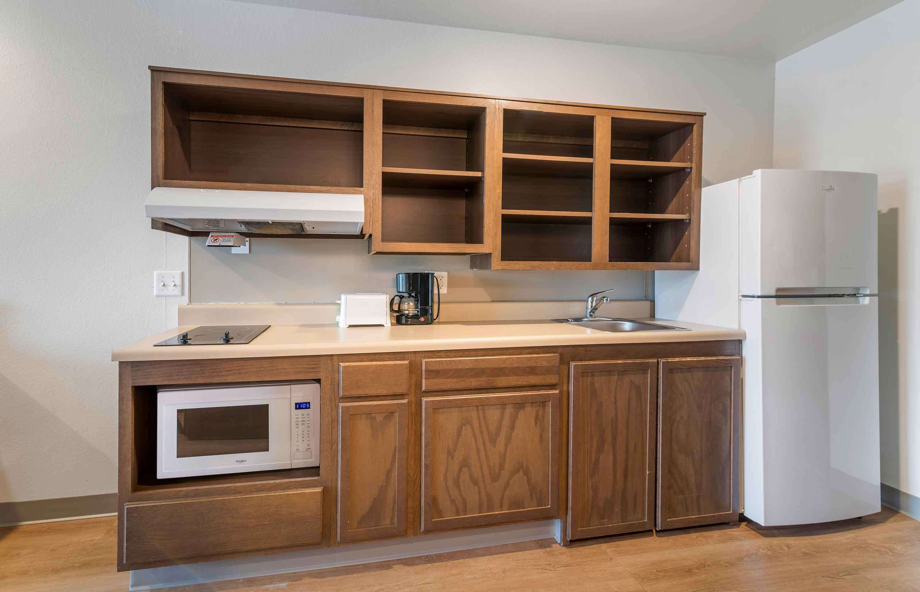 A compact kitchen with wooden cabinets, a built-in microwave, a coffee maker, and a refrigerator.