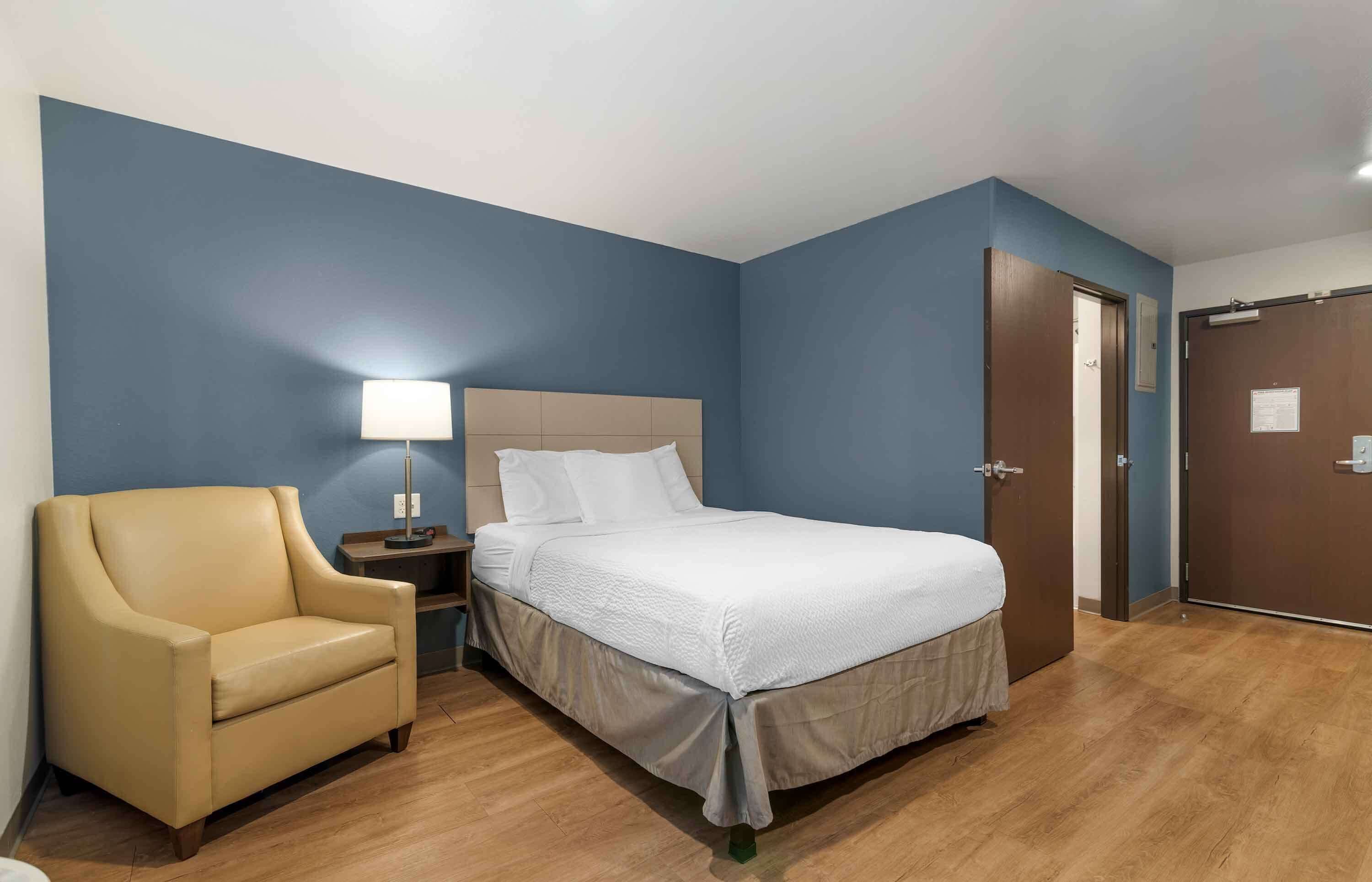 Een hotelkamer met een bed, een stoel, een nachtkastje en een lamp.