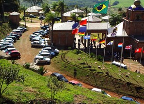 A parking area with multiple cars and flags, a building with a clock tower, and a grassy area with trees.