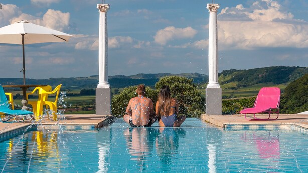 A couple sitting by a pool with a view of hills. - Hotel Mosteiro Brotas (Brotas)
