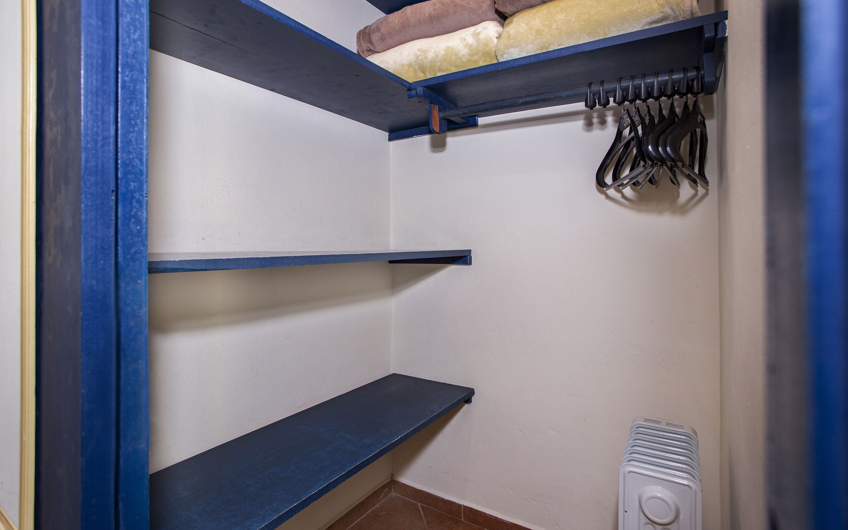 A closet with blue shelves, a radiator, and hanging clothes.