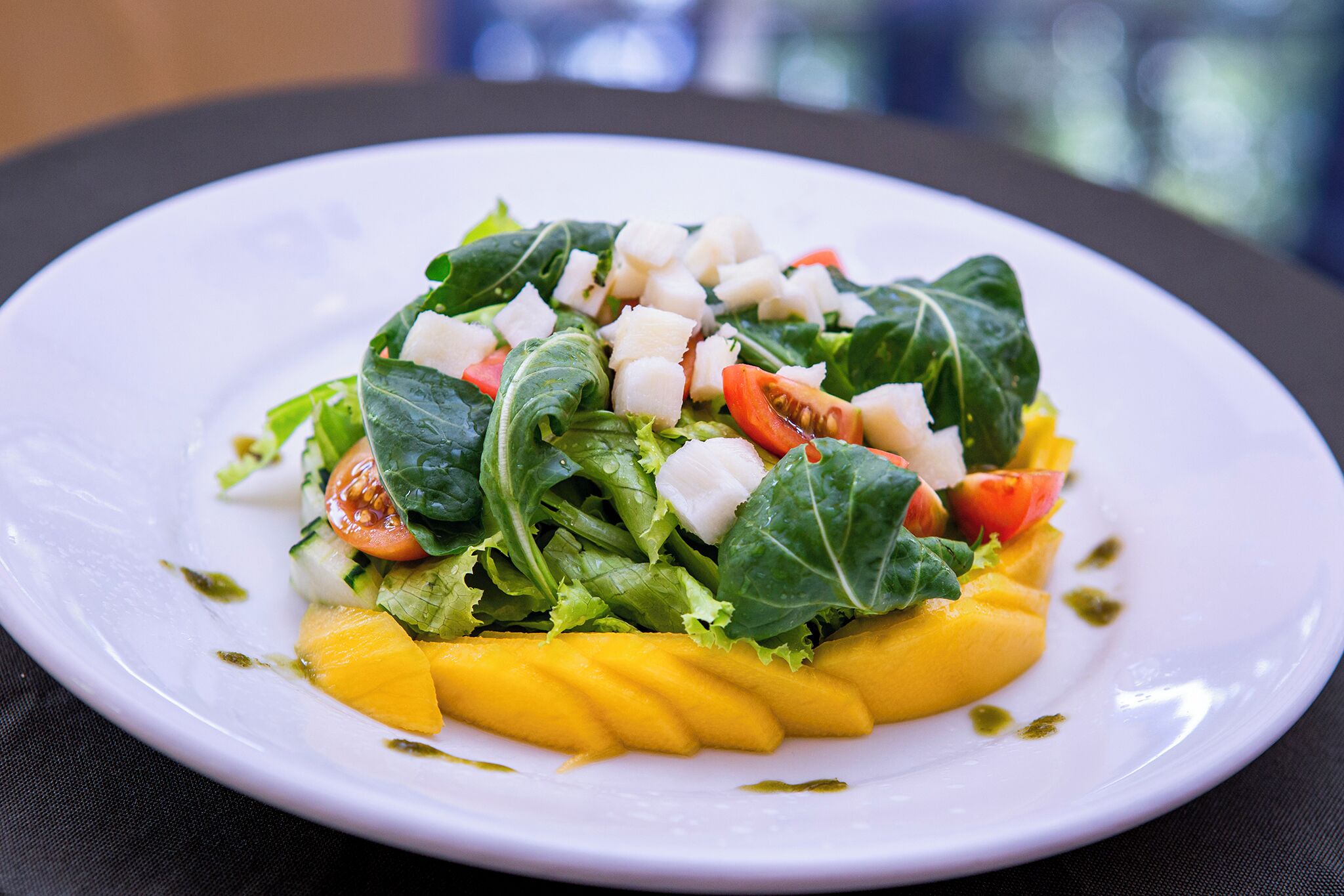 Un plato de ensalada fresca con hojas verdes, tomates y rodajas de mango.