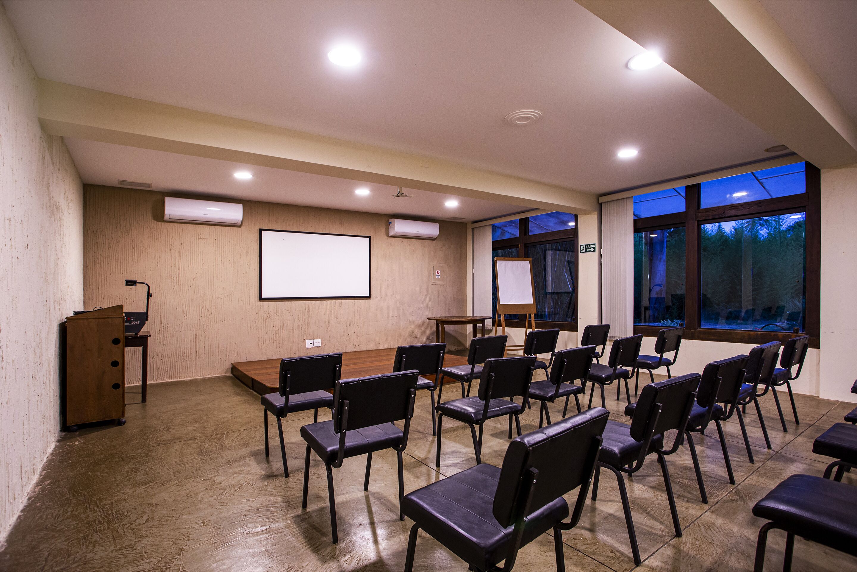Un salón de conferencias con una pantalla de proyector, una pizarra y una gran mesa.