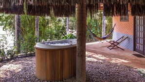 Un bain à remous sous un toit de chaume, un hamac et un bâtiment en briques avec une fenêtre.