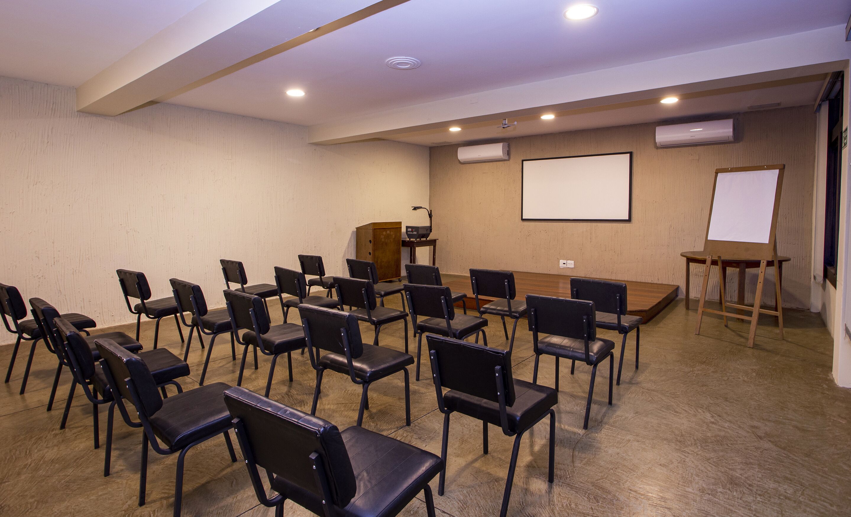 A conference room with rows of chairs, a podium, a projector screen, and an easel.