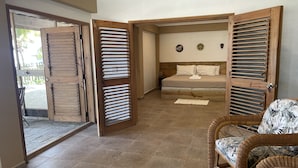 A room with a bed, a wicker chair, and a wooden door with louvered panels. - Hotel Guanaja (Guanaja)