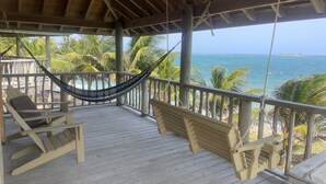 A wooden deck with a hammock, two chairs, and a view of the ocean. - Hotel Guanaja (Guanaja)