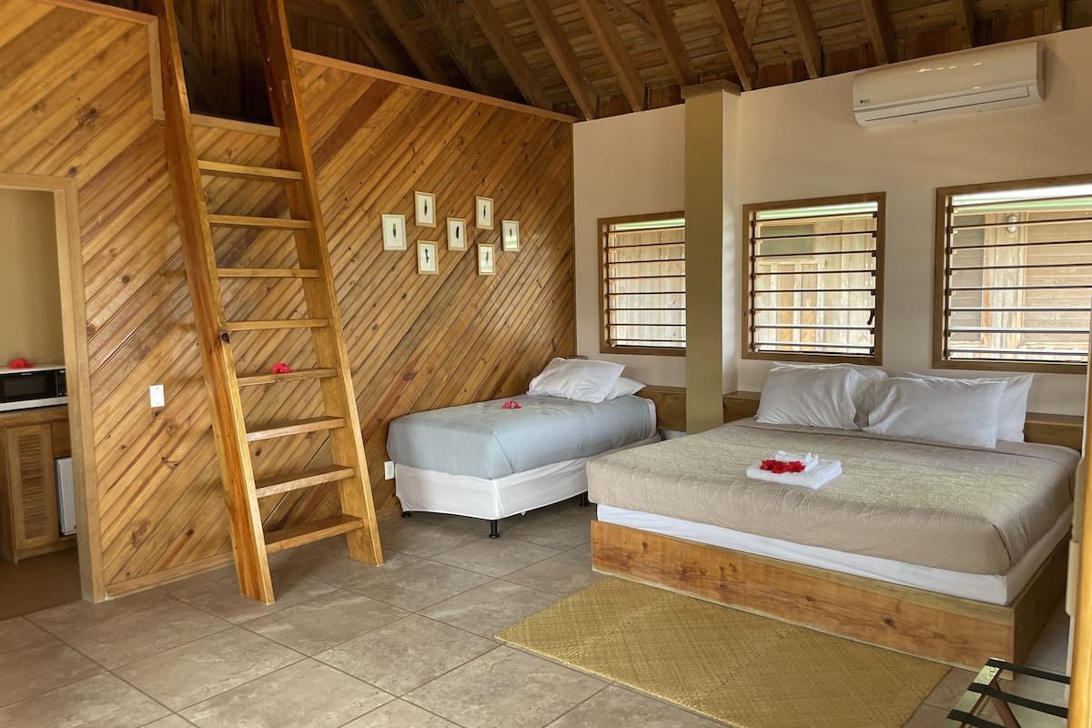 A bedroom with two beds, a wooden ladder, and a wall with framed pictures.