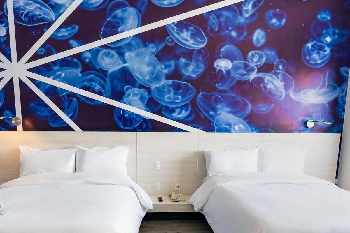 A hotel room with two beds, a modern geometric wall art, and a wooden floor.