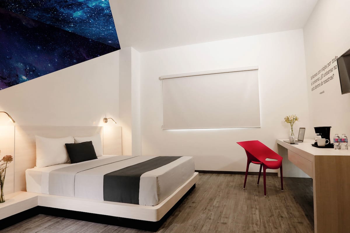 A modern hotel room with a bed, desk, chair, and a TV mounted on the wall.