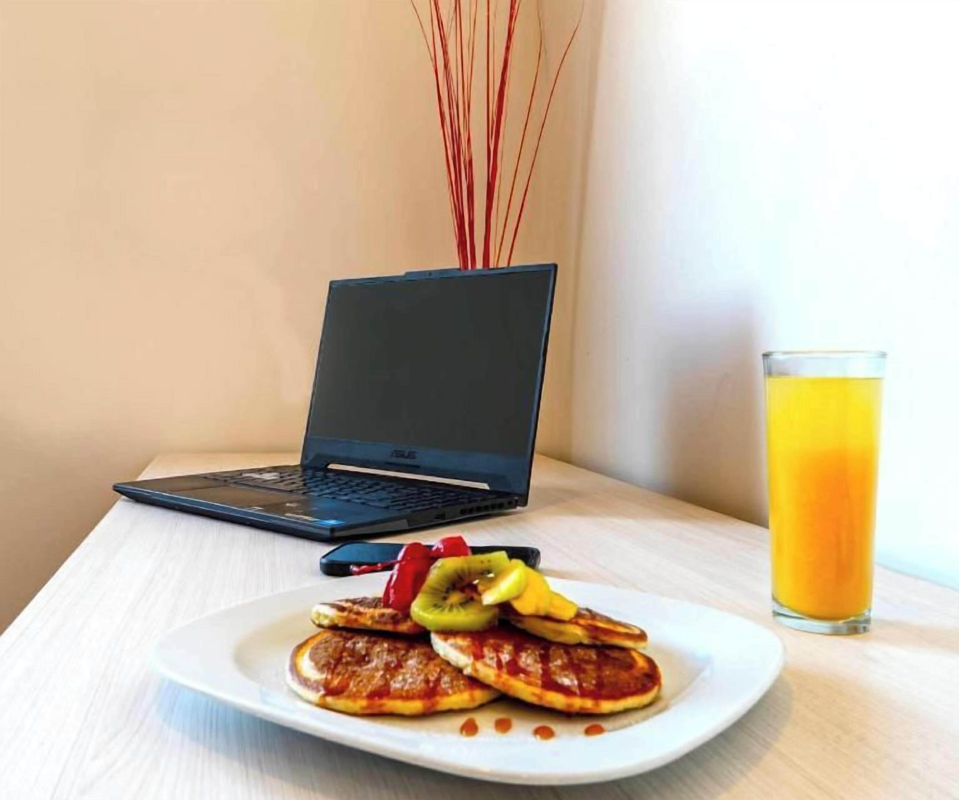 A laptop on a table with a plate of food and a glass of orange juice.
