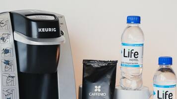 Une machine à café Keurig, deux bouteilles d’eau de la marque Life Hotel, un sachet de café Caffenio et une dosette de café.