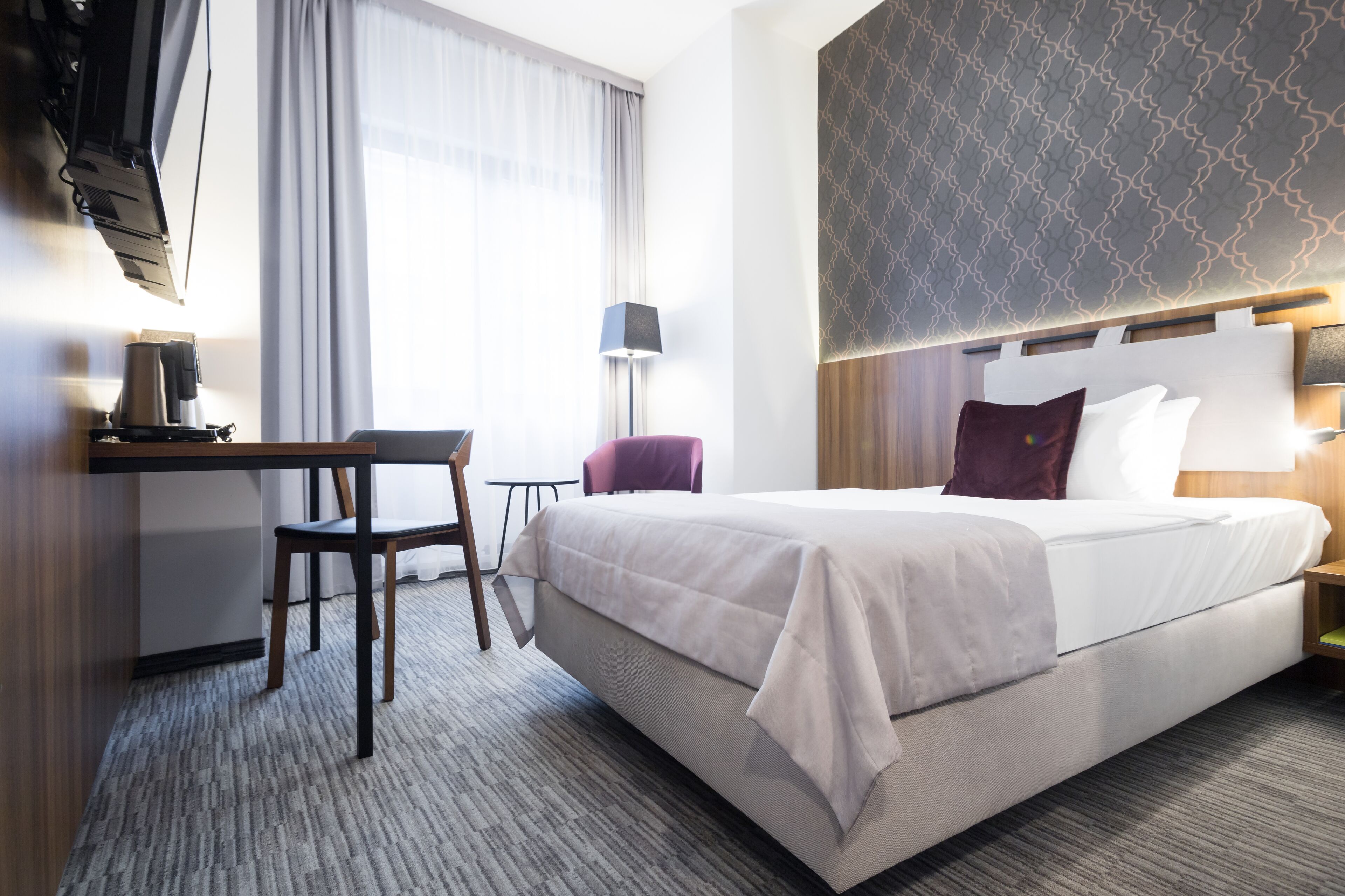Una habitación de hotel con una cama grande, un escritorio con silla, una cafetera y una lámpara.