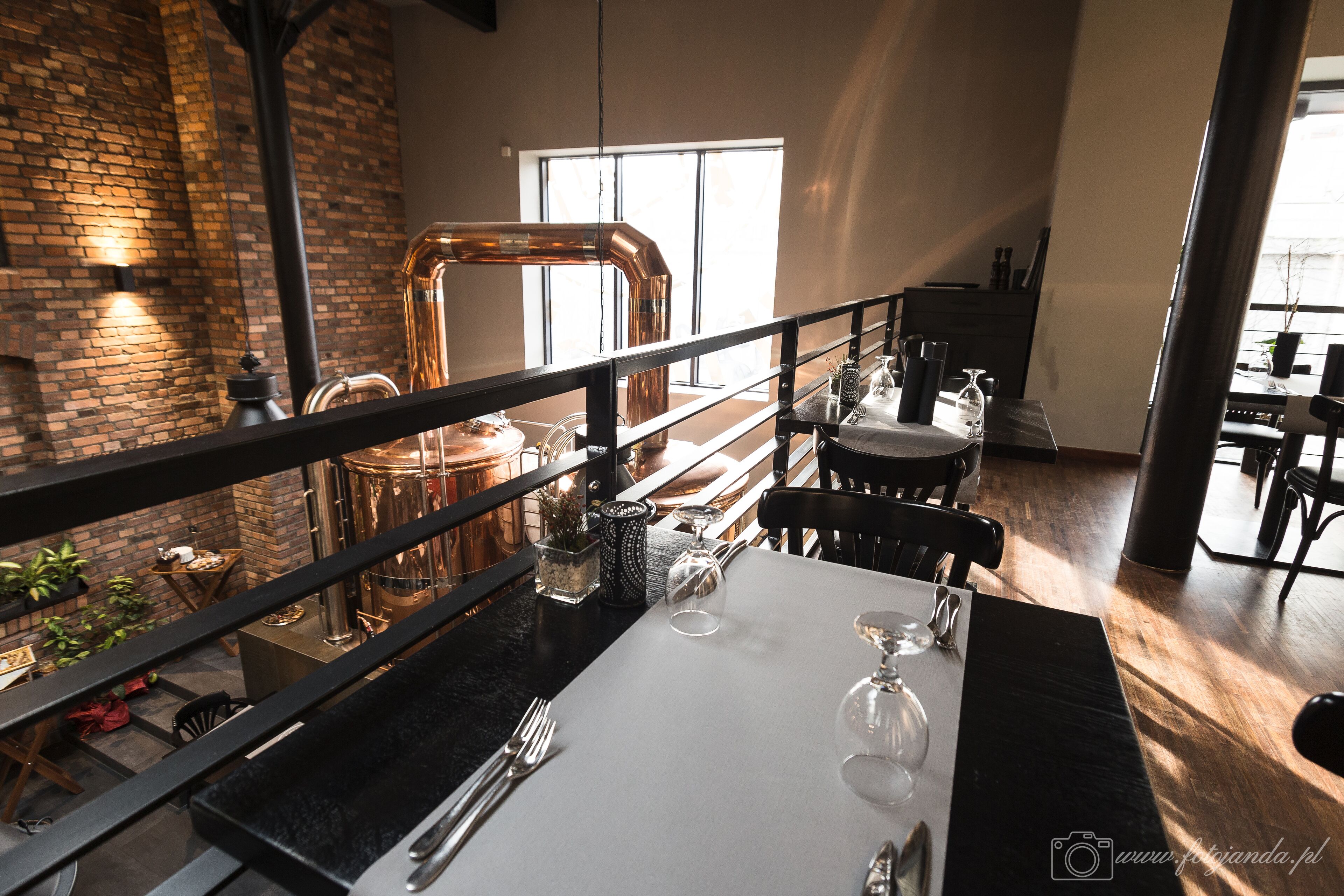 A dining area with a table set for two, a brick wall, and a large window in the background.