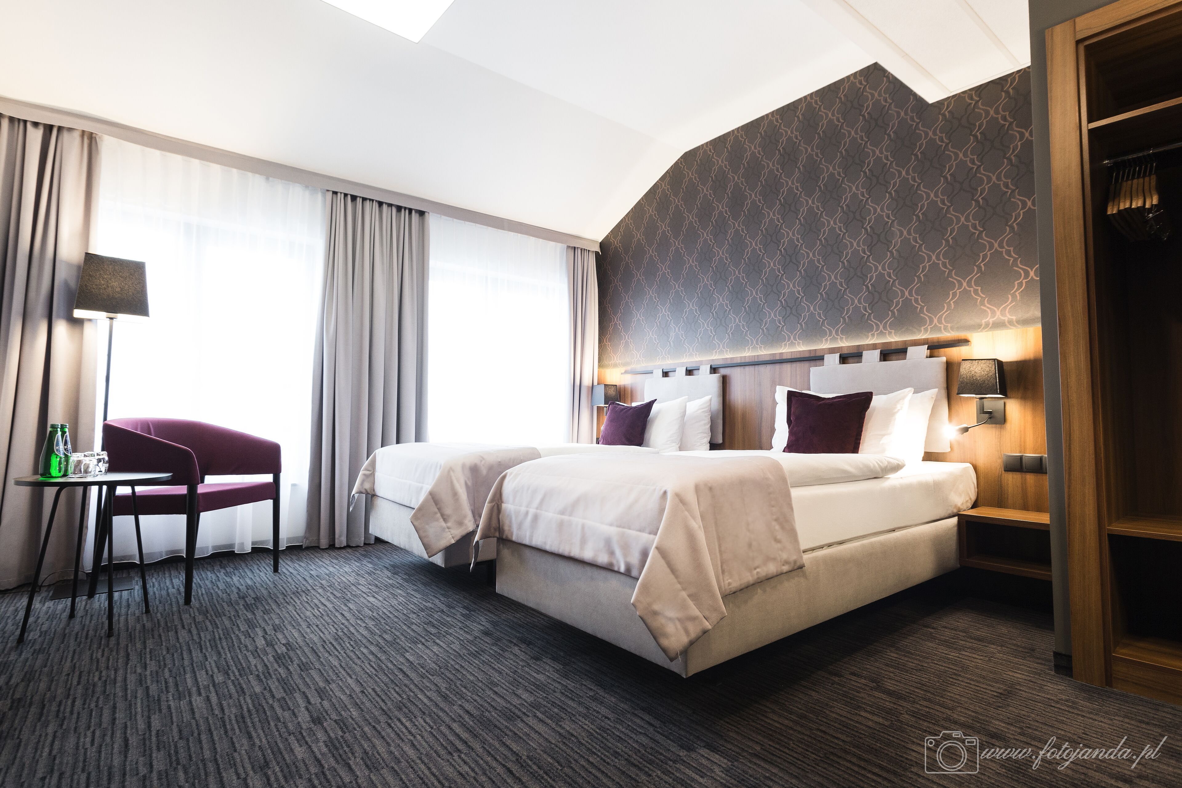A hotel room with a large bed, two bedside tables, a desk with a chair, and a wardrobe.