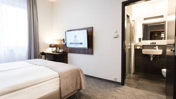 Habitación de hotel con cama, escritorio, televisor mostrando 'Best Western' y baño con lavabo y espejo.