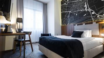 Habitación de hotel con cama, escritorio con silla, lámpara, cafetera y un mapa de pared grande.