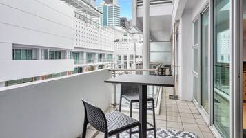 Un balcón con una mesa y sillas, un tapete estampado y vistas de un paisaje urbano con edificios modernos.