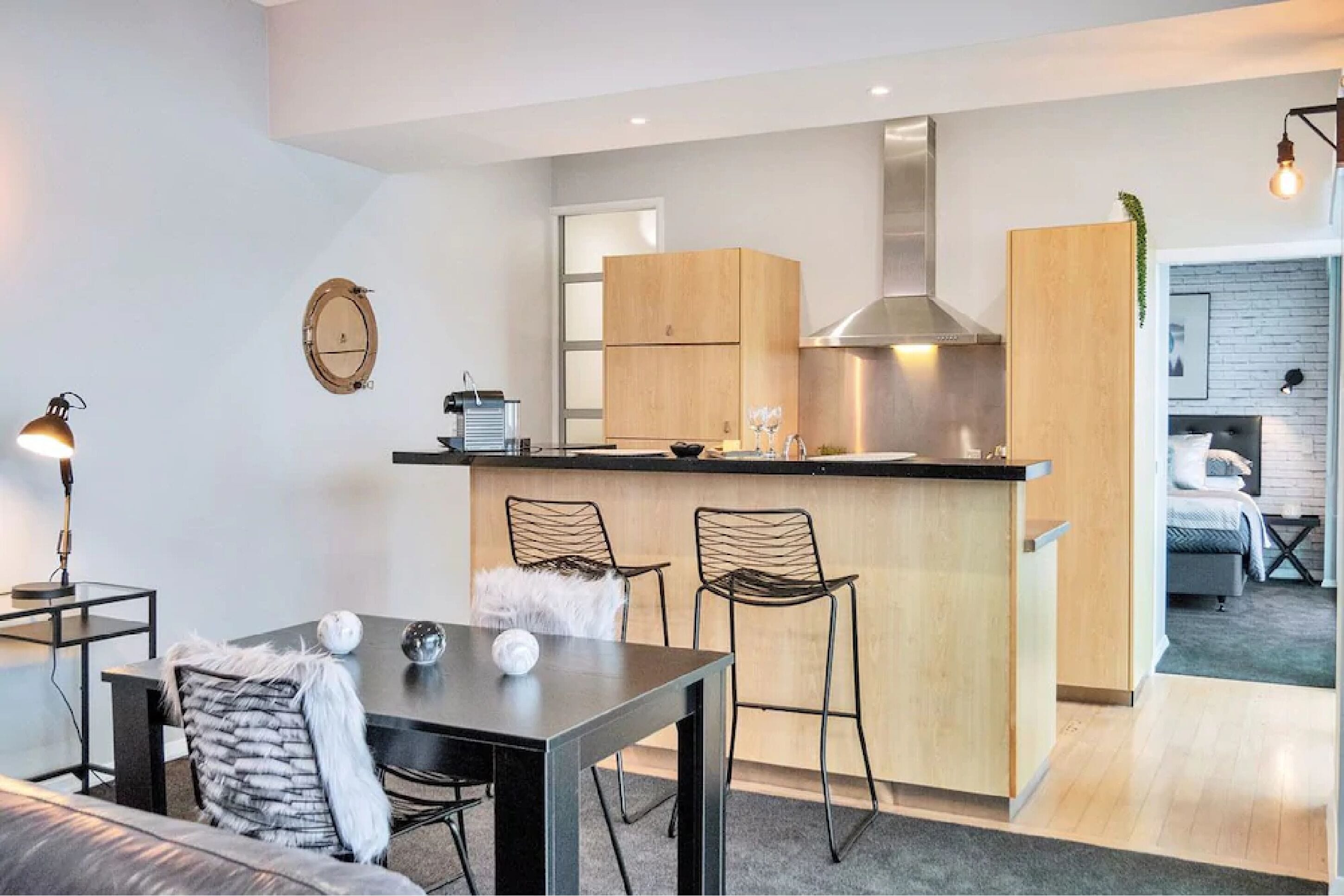 A modern kitchen with wooden cabinets, a stainless steel range hood, and a small island with bar stools.