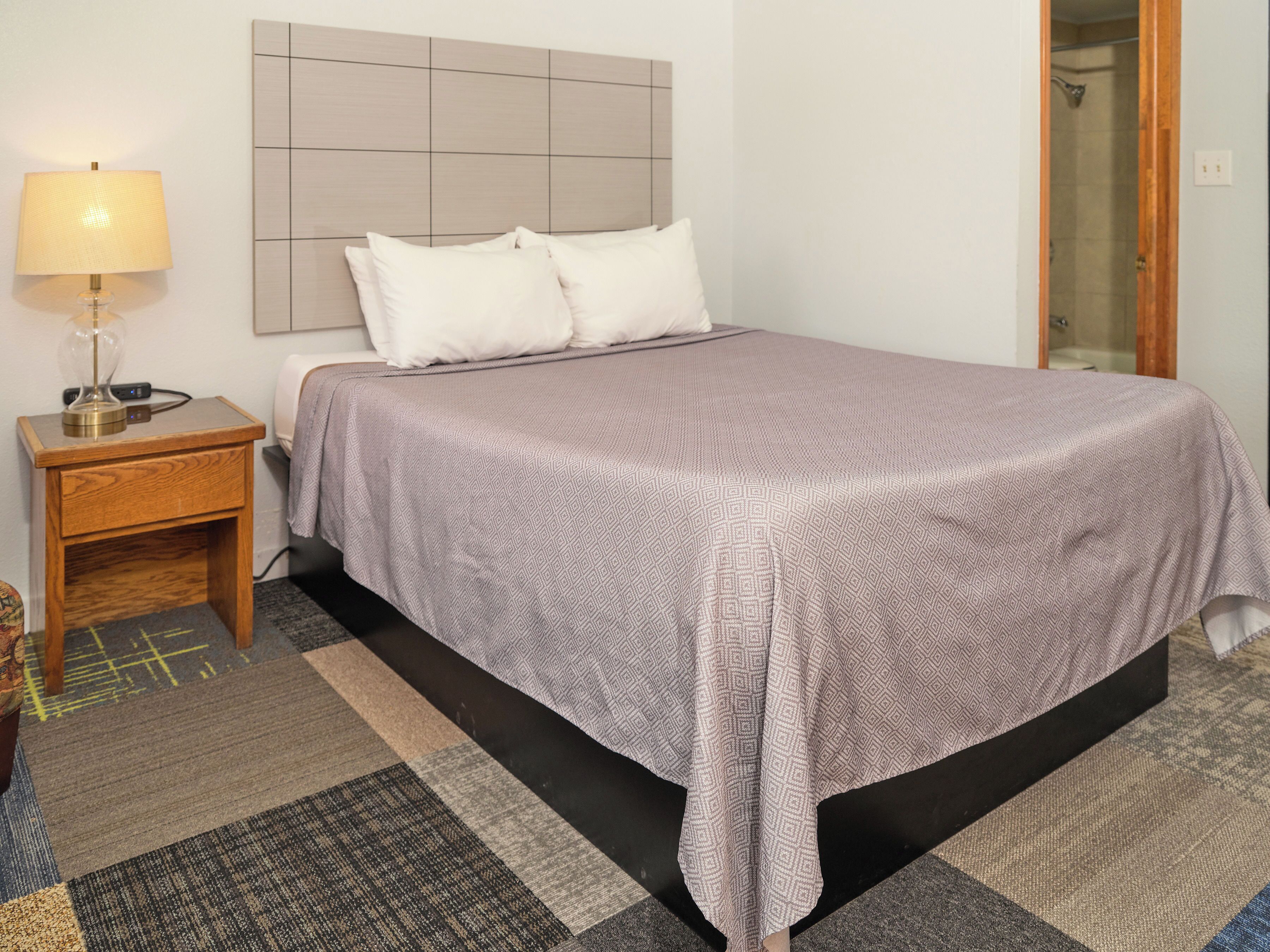 A neatly made bed with a patterned bedspread, a bedside lamp, and a small wooden nightstand.