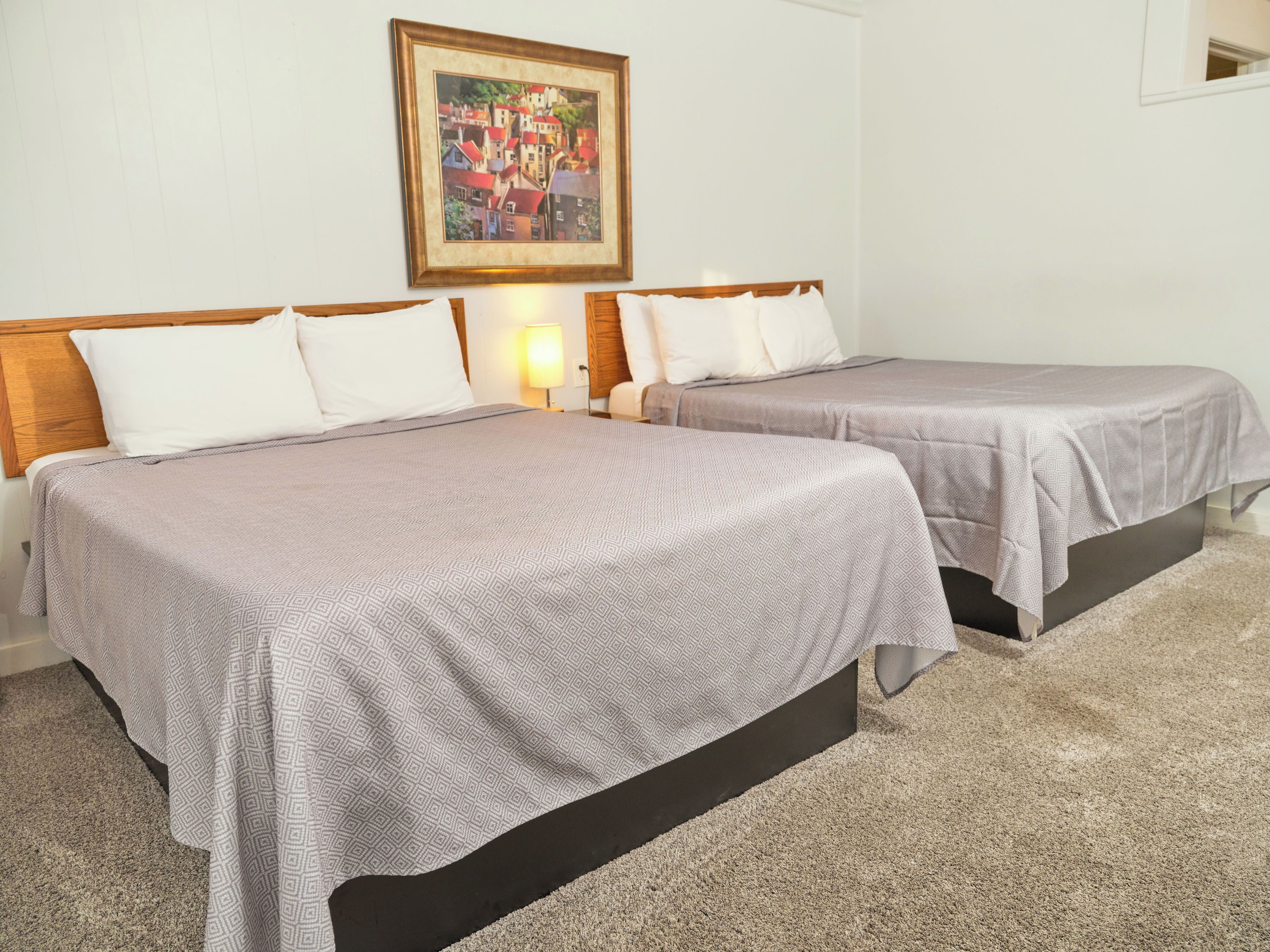 A hotel room with two single beds, a wooden headboard, a beige carpet, and a framed picture on the wall.
