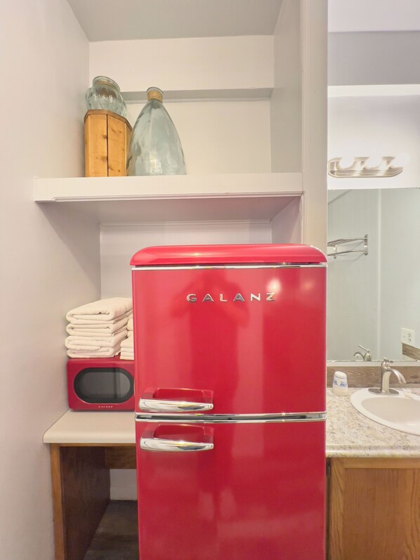 A red Galanz refrigerator in a bathroom with a sink and mirror. - The Oakwood Inn (Sterling)