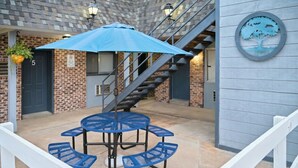 A patio area with a round table and blue chairs, a blue umbrella, and a staircase. - The Oakwood Inn (Sterling)