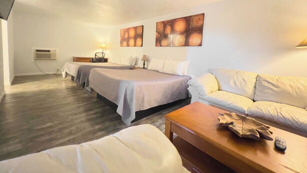A hotel room with two beds, a sofa, a wooden coffee table, and a flat-screen TV mounted on the wall. - The Oakwood Inn (Sterling)