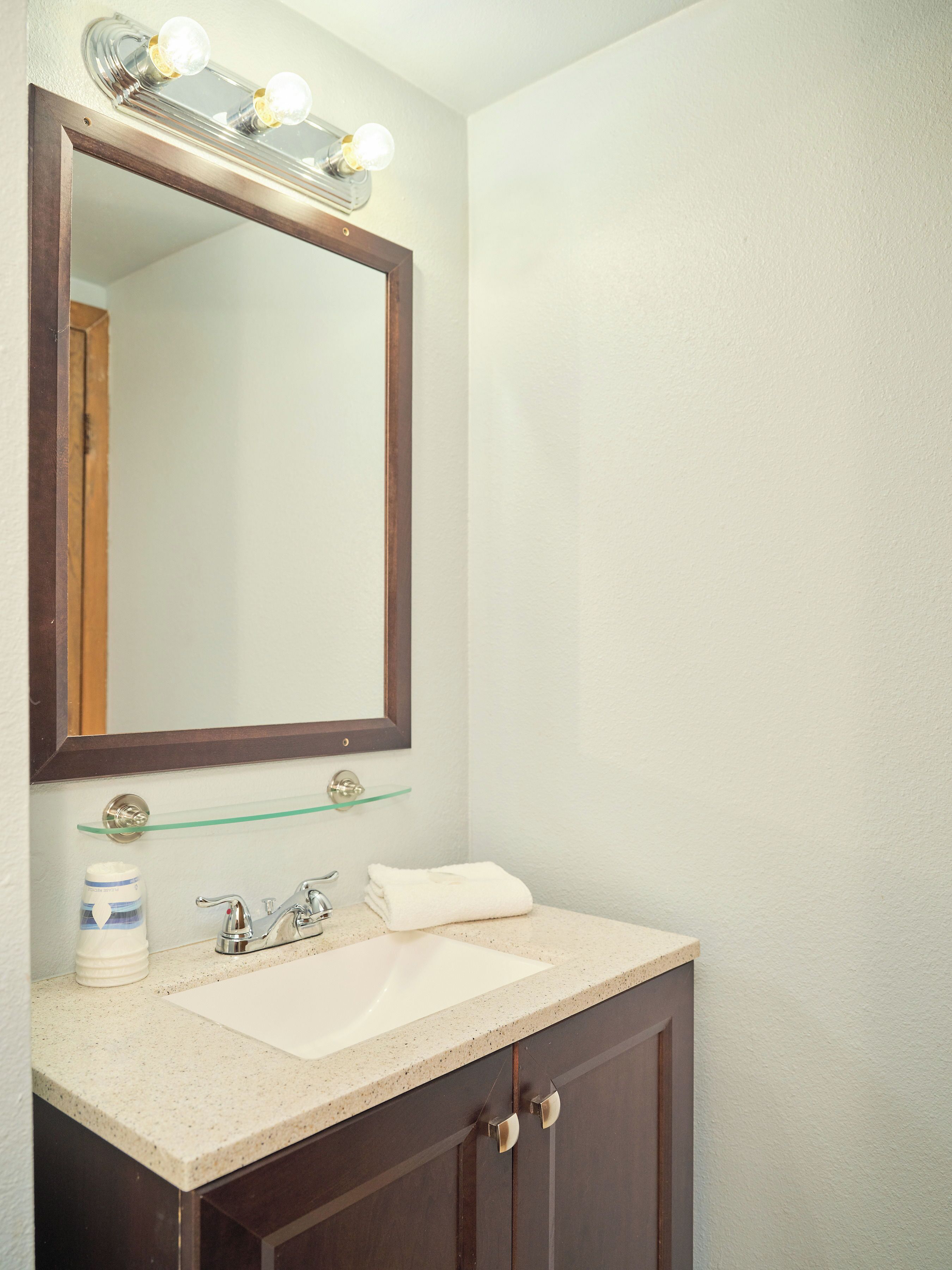 A bathroom with a large mirror, a sink, and a glass shelf above the sink.