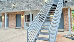 A building with a brick facade, numbered doors, and a metal staircase leading to an upper level. - The Oakwood Inn (Sterling)