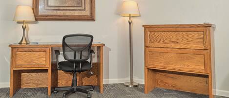 A hotel room with a wooden desk, two lamps, a chair, a TV, and a framed picture on the wall.