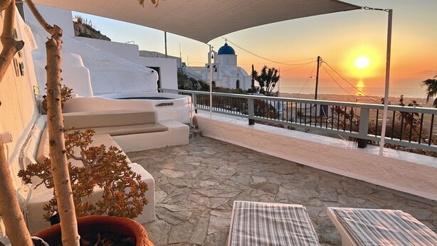 A terrace with stone flooring, a white building with a blue dome, and a sunset view.