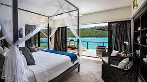 A bedroom with a four-poster bed, a balcony with a view of the sea, and a seating area with a sofa. - The BEST Wedding Spot! 2 pools, gym, beachfront & MUCH MORE! (St. Thomas)