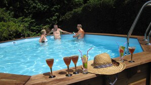 Una terraza de madera con piscina, rodeada de follaje.
