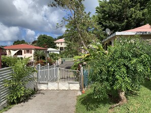 A gated entrance to a residential area with houses, a gate, and lush greenery.