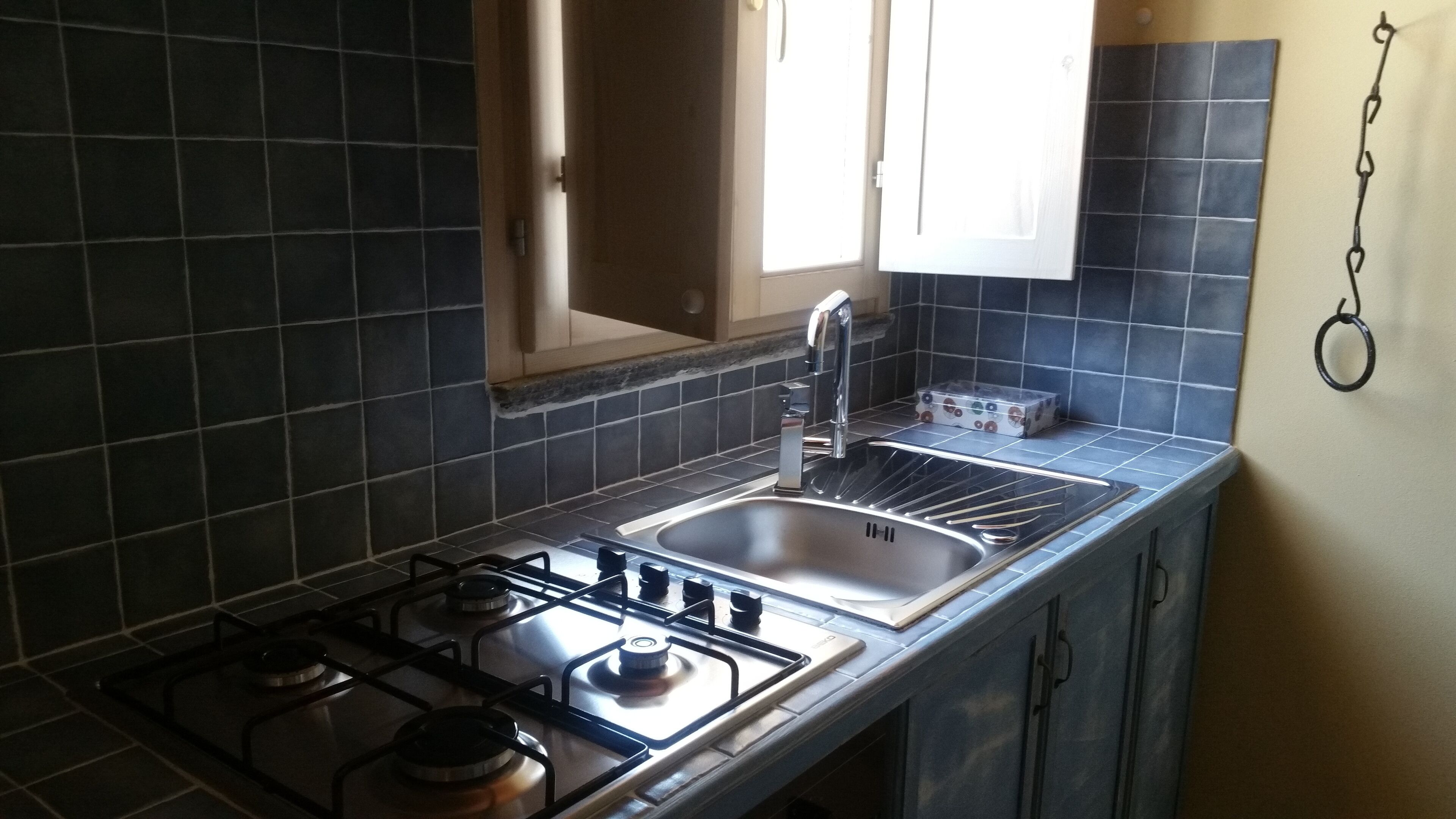 Une cuisine avec des carreaux de couleur sombre, une cuisinière à gaz, un évier et une fenêtre donnant sur un beau paysage.