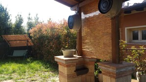 Estructura al aire libre de ladrillo con una parrilla de metal, un banco de madera y una planta en maceta.