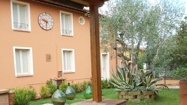 Un edificio con jardín, que incluye una pérgola, plantas en macetas y un árbol grande.