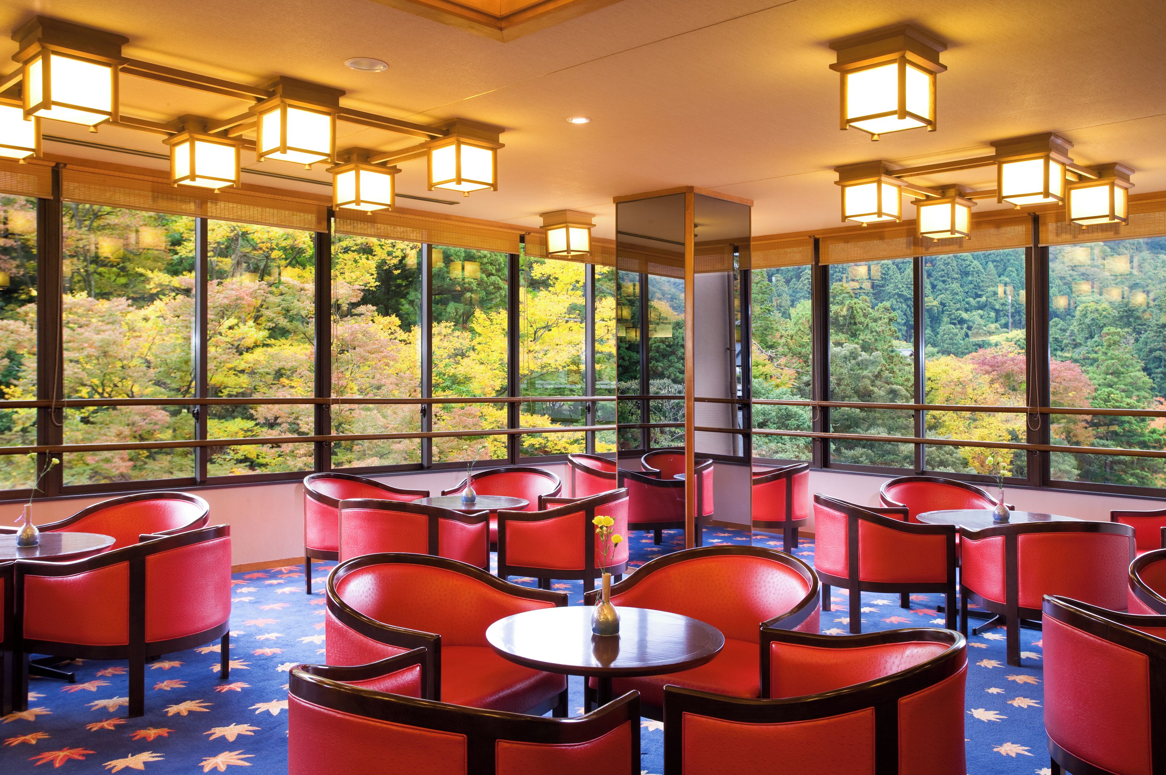 A hotel room with large windows, red chairs, and tables.
