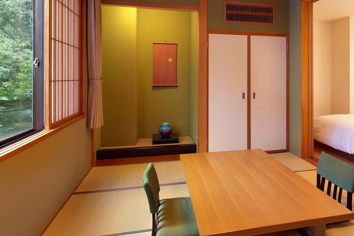 Una habitació tradicional japonesa amb tatami, una taula baixa i un llit amb capçalera de fusta.