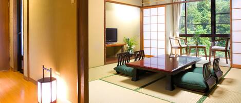 A traditional Japanese room with tatami flooring, a low table with cushions, and a television on a stand.