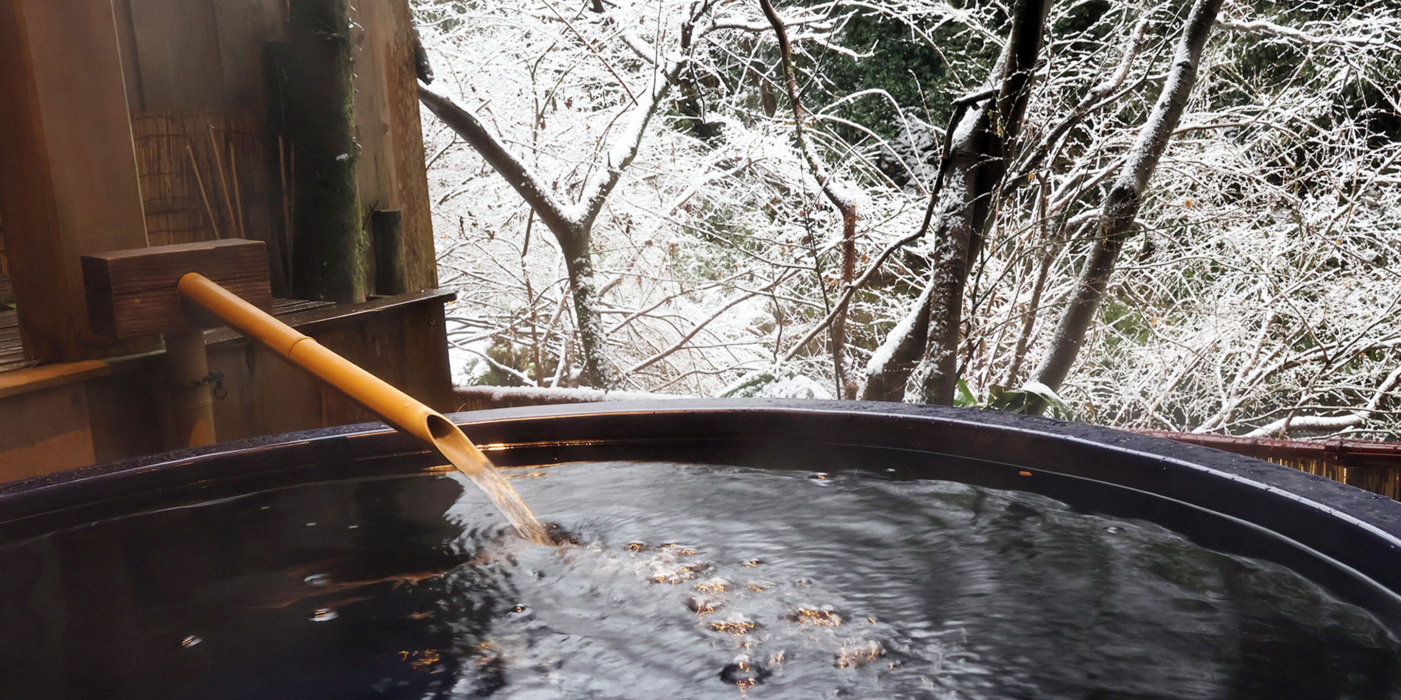 A hot tub with a wooden spoon inside, surrounded by snow-covered trees.