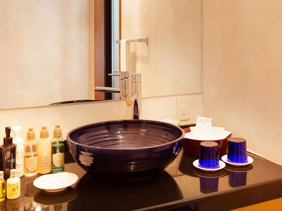 Un baño con un lavamanos azul oscuro grande, un espejo y distintos artículos de aseo en la encimera.