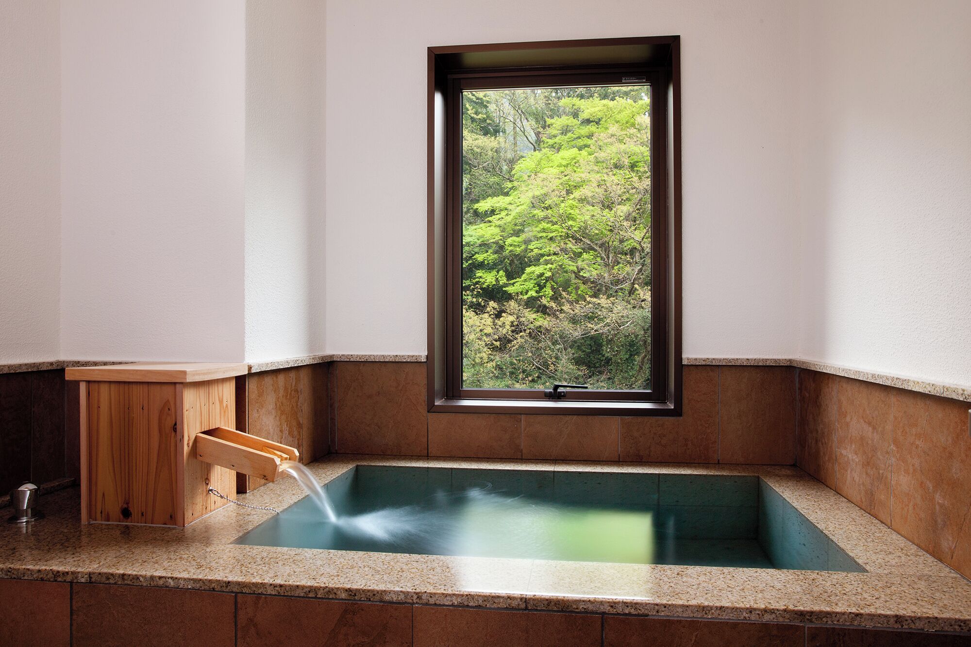 Un bain thermal avec un banc en bois, une fenêtre donnant sur la forêt et un sol carrelé.
