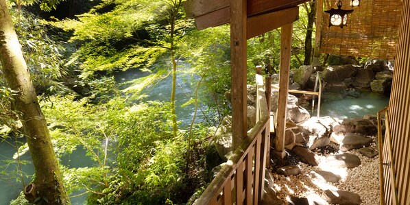 A wooden deck overlooking a natural hot spring surrounded by lush greenery. - Kagari Kisshotei (Kaga)