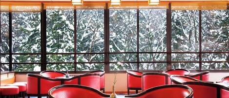 Habitación de hotel con ventanas amplias, sillones tapizados en rojo y una mesa redonda.